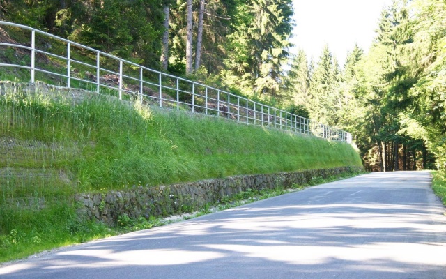 Wysokie oddzielenie drogi i ścieżki rowerowej stromym zboczem w Prášilech na Szumawie